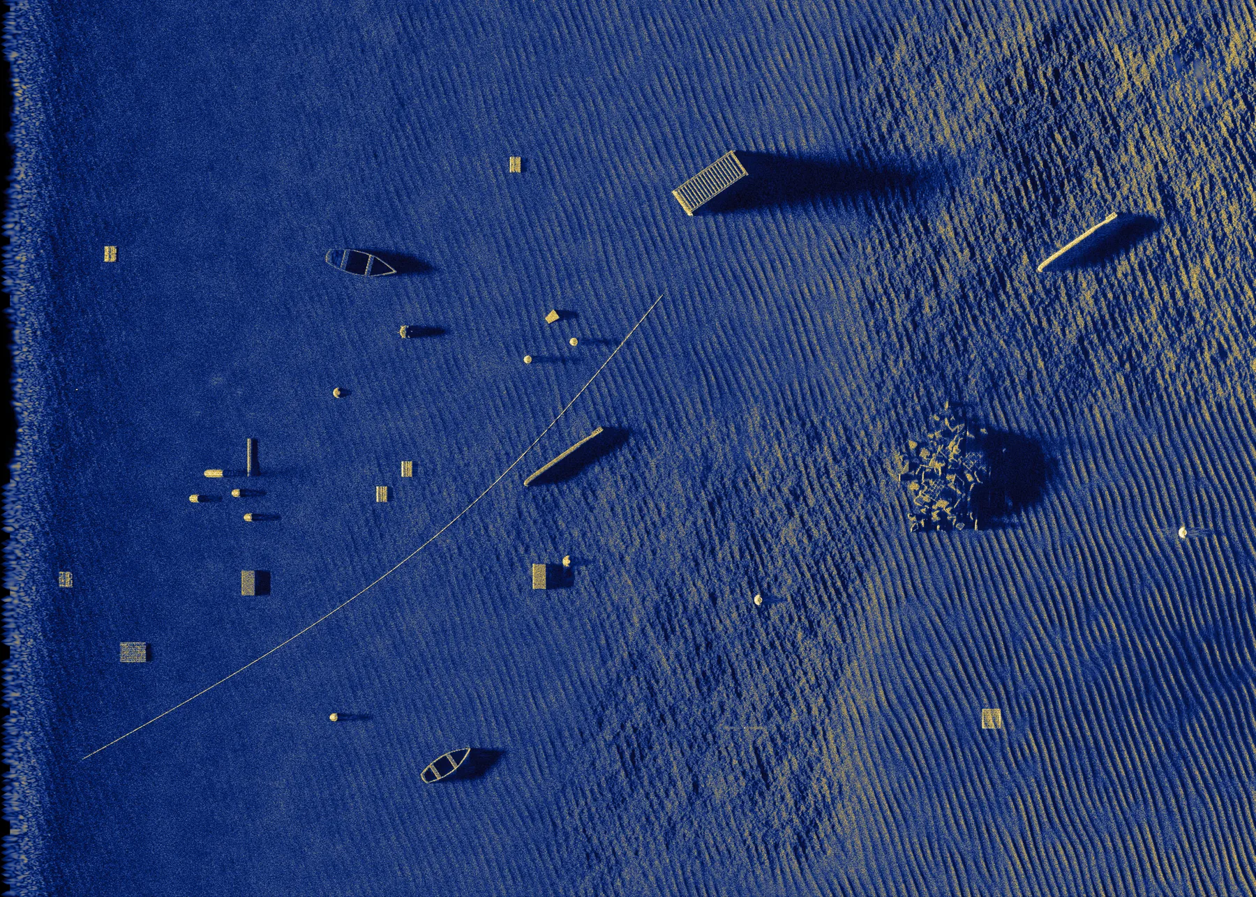 A simulated synthetic aperture sonar image of a seafloor scene holding boat hulls, a torpedo shape, containers, barrels, truss frames, a cable and a rock outcrop over rippled sand, with every shadow falling to the right, away from the track along the left edge